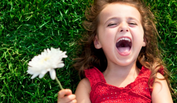 Niña sonrie en el césped con flor en la mano